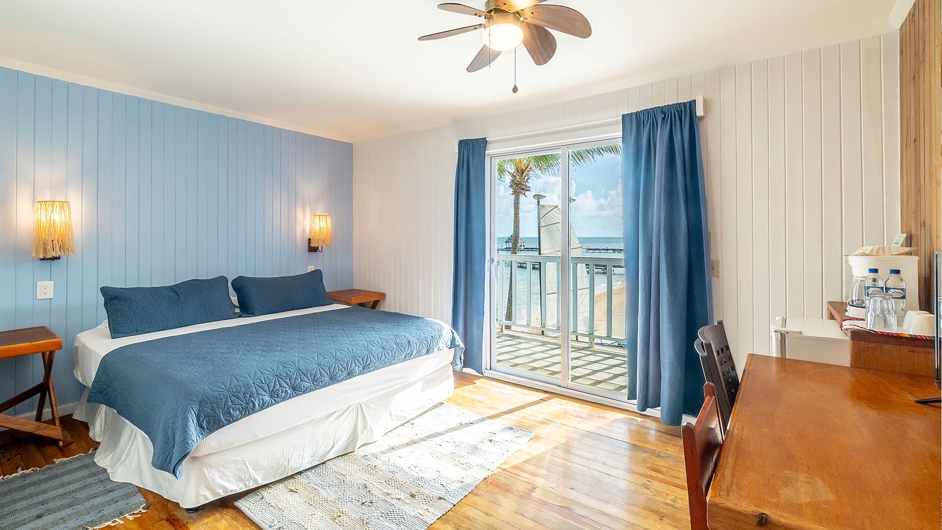 A cozy beachside hotel room featuring a king-size bed, wooden floors, and a balcony with ocean views.