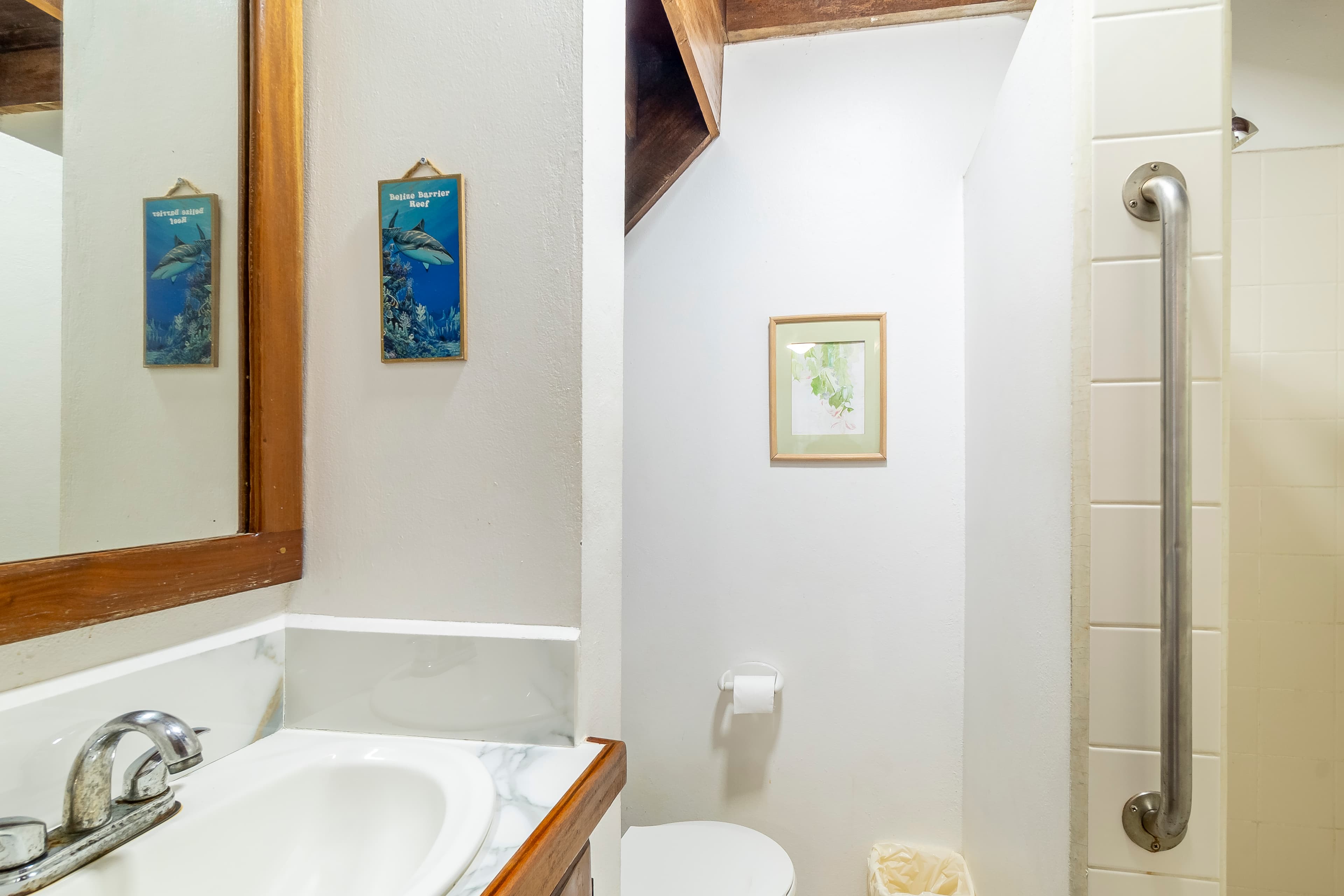 Clean, white-tiled bathroom featuring a marble-topped vanity with a chrome faucet, a large mirror, and a modern walk-in shower with a stainless steel safety grab bar.