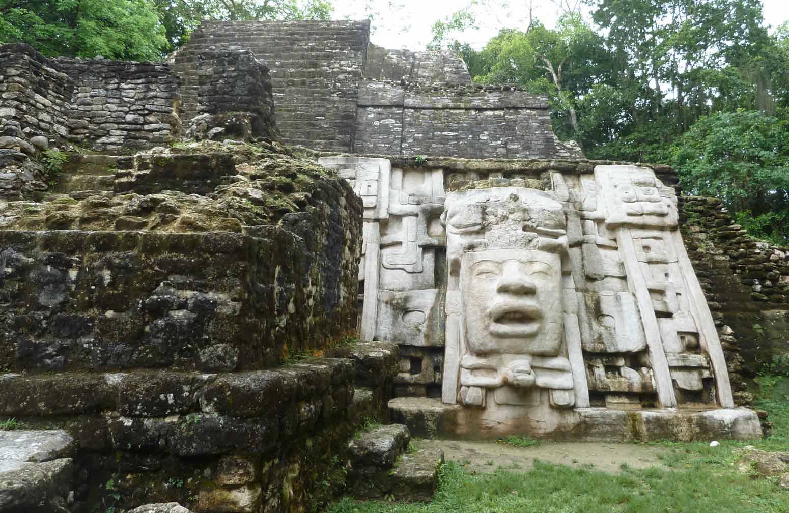 Ancient stone structure featuring a large, carved face amidst overgrown ruins.