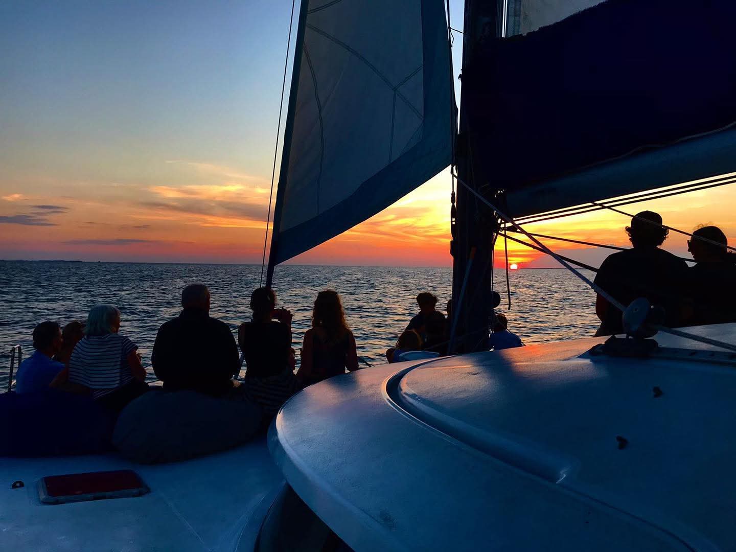 Silhouetted figures sit on a boat as a vibrant sunset reflects on the ocean.
