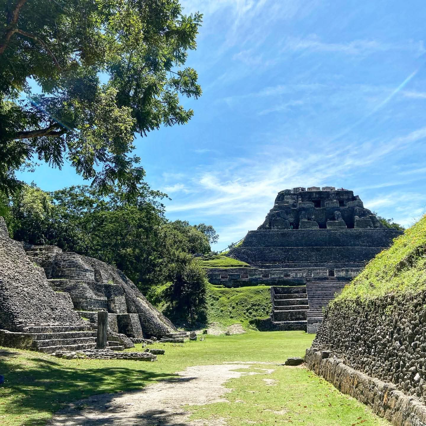 Ancient ruins of a Mayan pyramid surrounded by lush greenery under a bright blue sky.