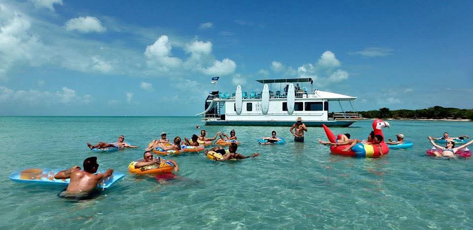 People relax in the clear turquoise water, floating on colorful rafts near a boat.