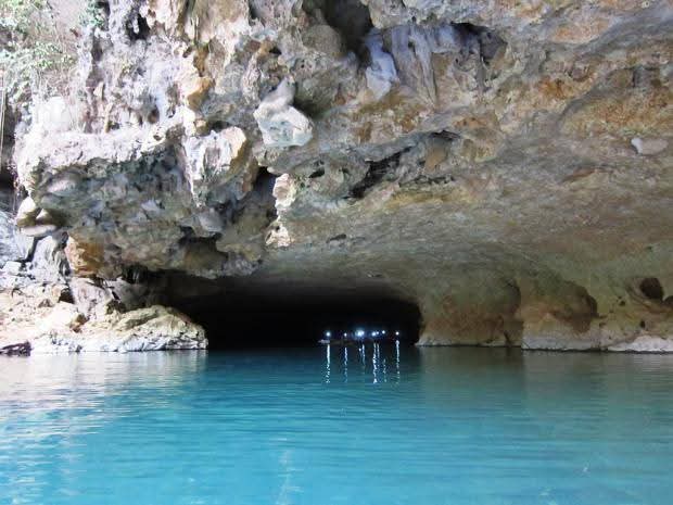 A serene underground cave with clear blue water reflecting lights from a small boat.