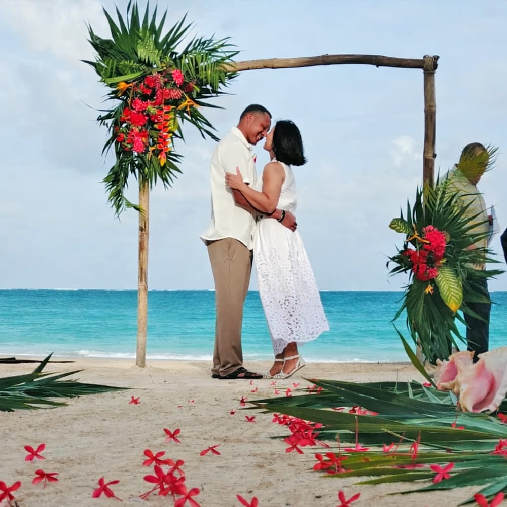 A couple shares a romantic moment under a floral arch on a beach.