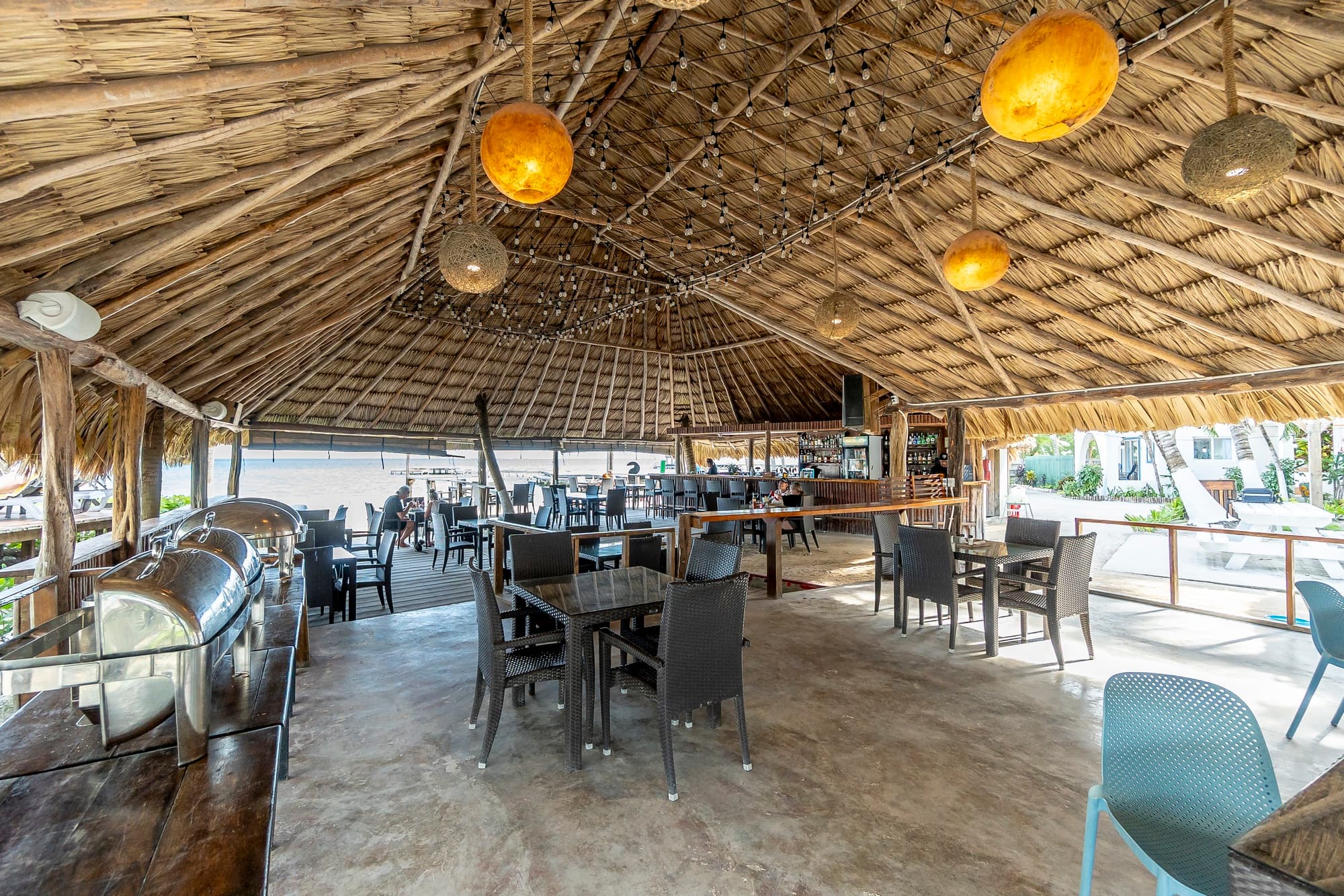 Interior of a tropical-themed restaurant with a thatched roof and empty tables.