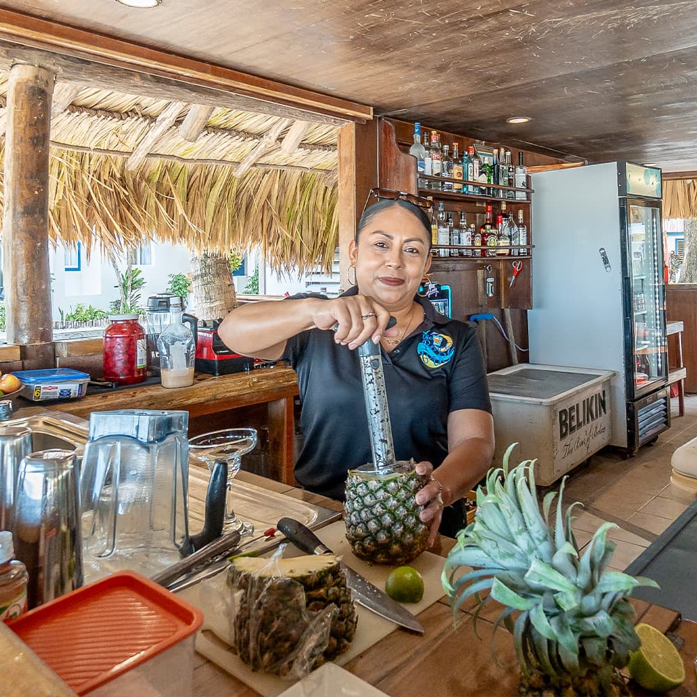 A bartender prepares a drink inside a tropical bar, using a pineapple as a cup.