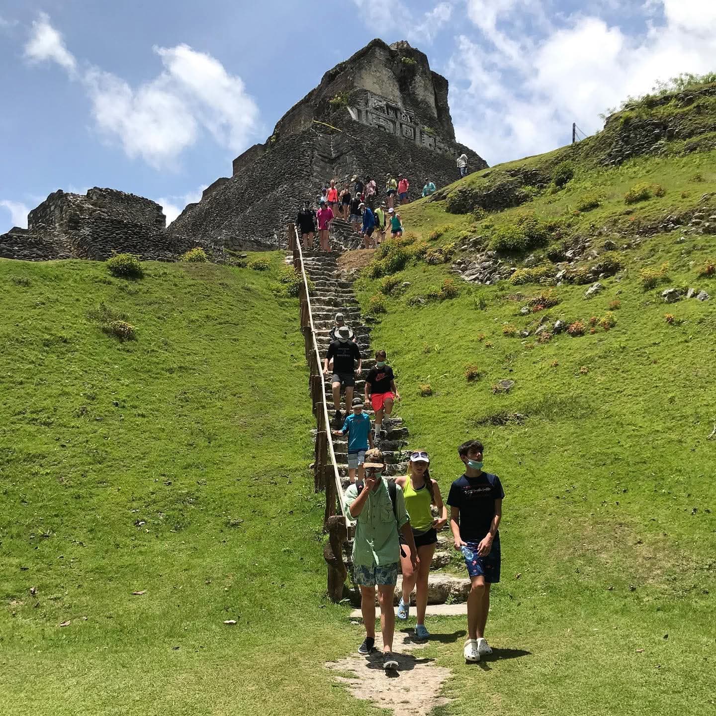 A group of hikers ascends stone steps towards a hilltop ruin under a blue sky.