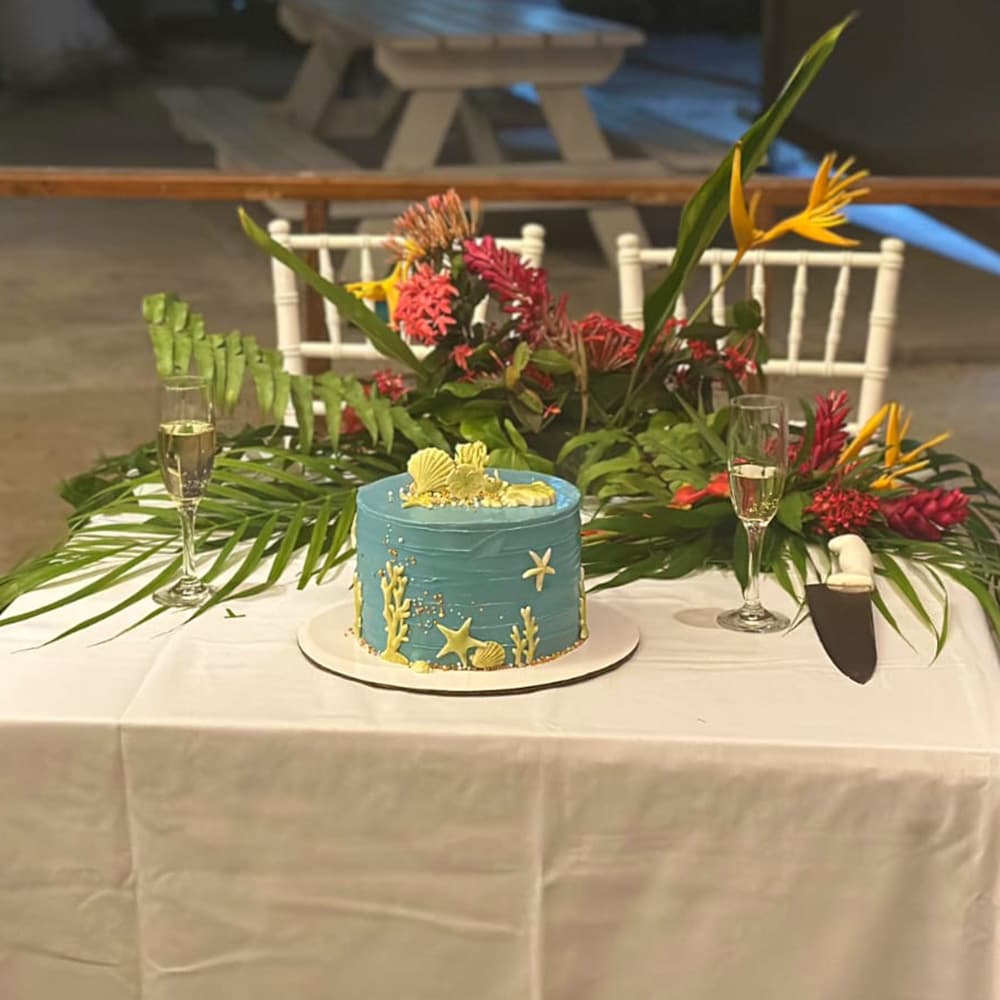 A decorative ocean-themed cake sits on a table adorned with tropical flowers and champagne glasses.
