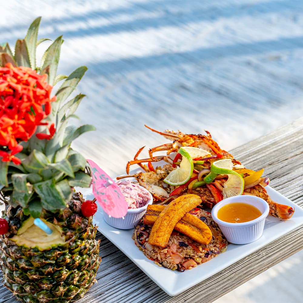 A colorful plate of seafood, plantains, rice, and sauces, next to a decorated pineapple.