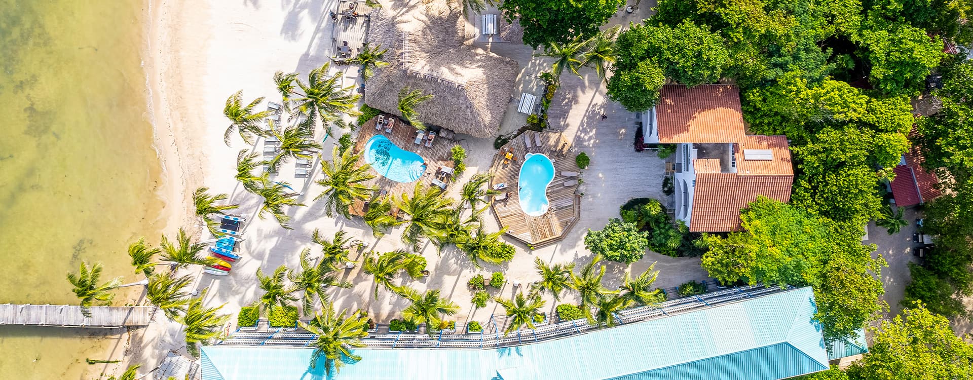 Aerial view of a tropical resort with pools, palm trees, and a sandy beach.