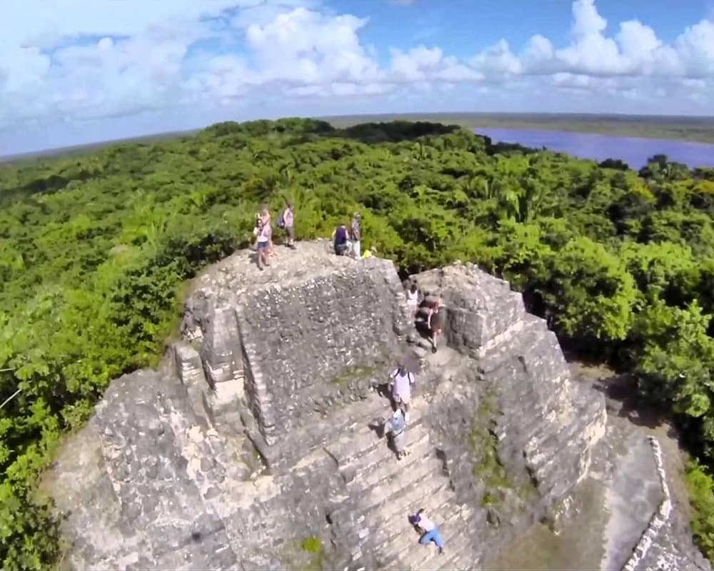 Aerial view of people exploring a Mayan pyramid surrounded by lush greenery.