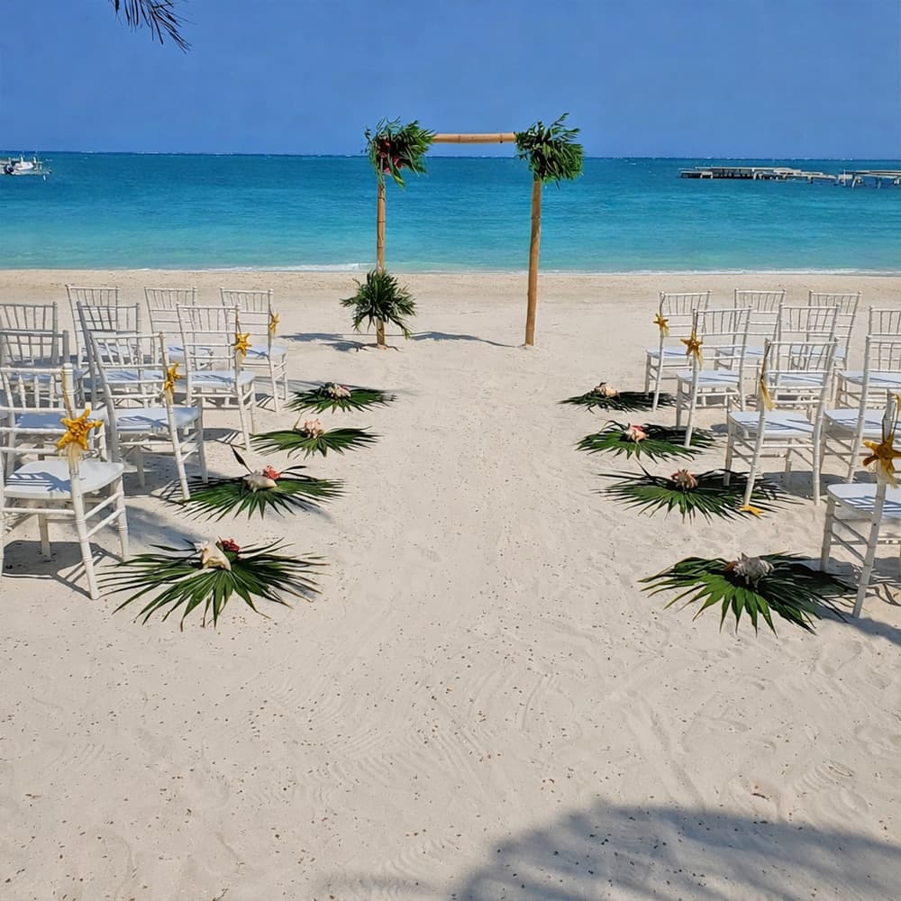 A beach wedding setup with white chairs and tropical decorations facing the ocean.